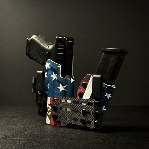 Compact tactical gun holster holding two pistols and magazines, wrapped in American flag fabric, on a dark surface.