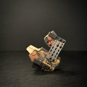Camouflage-patterned firearm holster with metal straps on a dark surface.