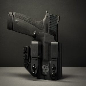 Semi-automatic pistol in a black holster with two magazine pouches attached to the sides, resting on a flat surface.