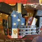 Close-up of a black handgun in a star-spangled holster with extra magazines on a distressed flag-patterned surface.